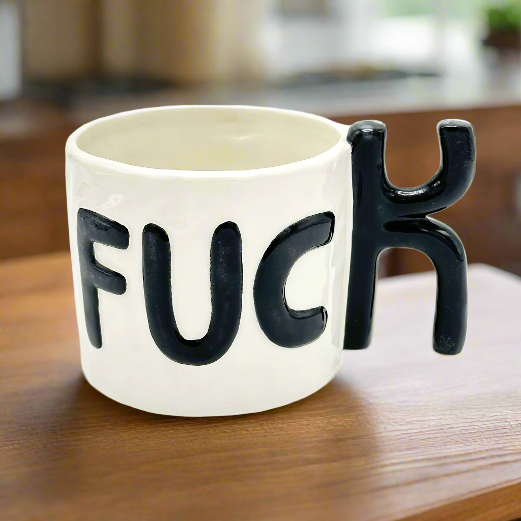 A white ceramic mug with the word 'FUCK' in black letters, designed with a handle shaped like the letter 'K'.