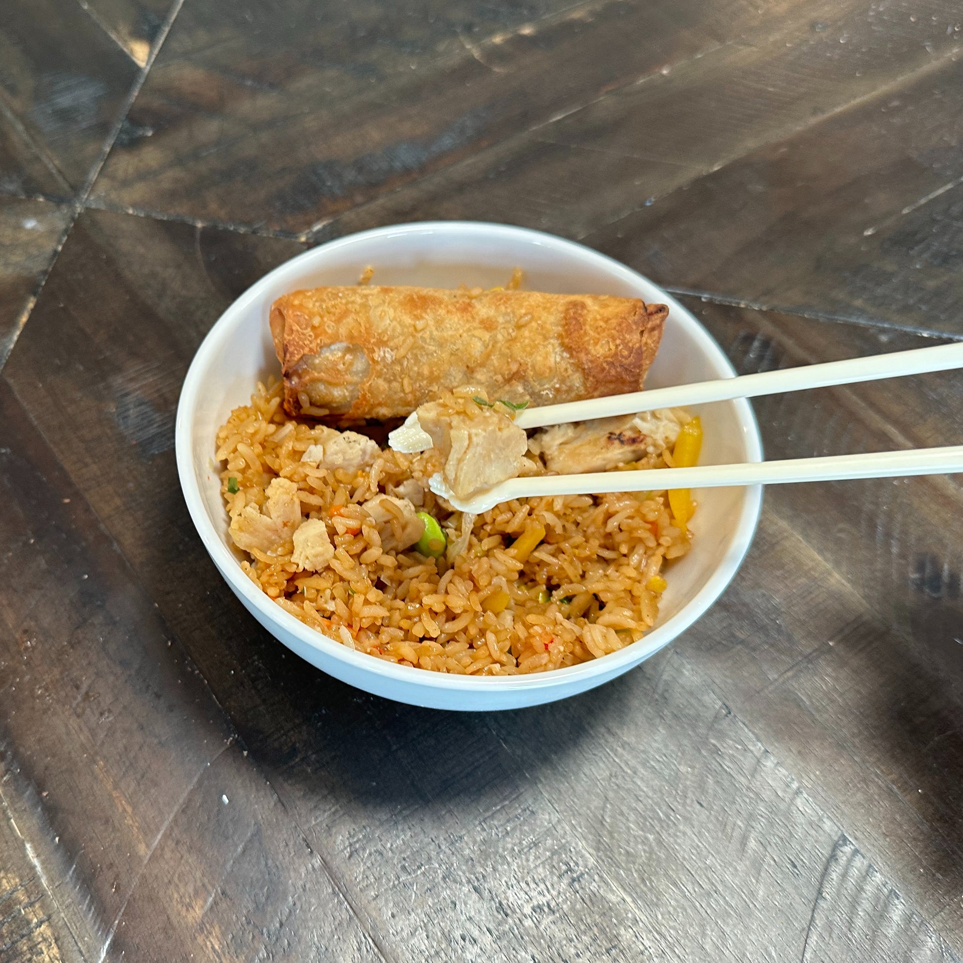 Bowl of fried rice with a spring roll and chopsticks on a metallic surface