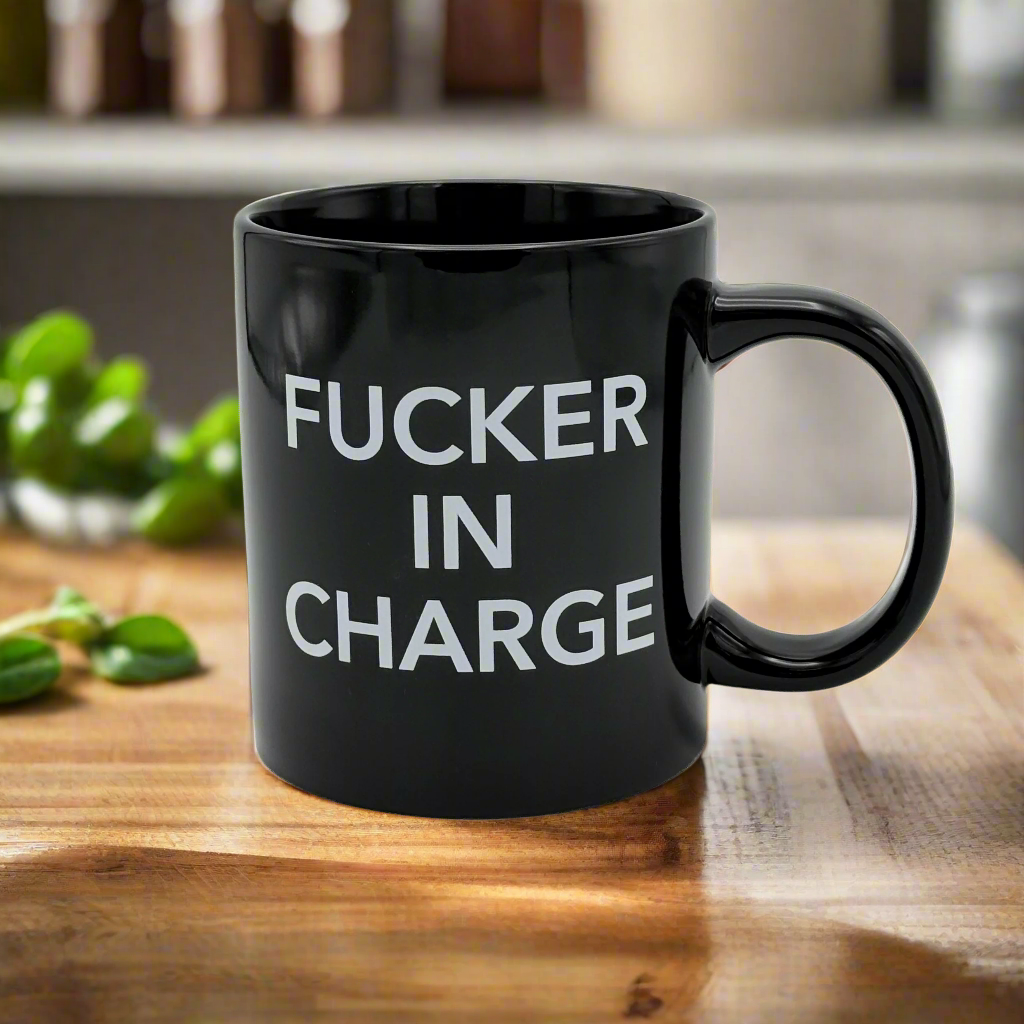 A black ceramic mug with the text 'FUCKER IN CHARGE' printed in white.