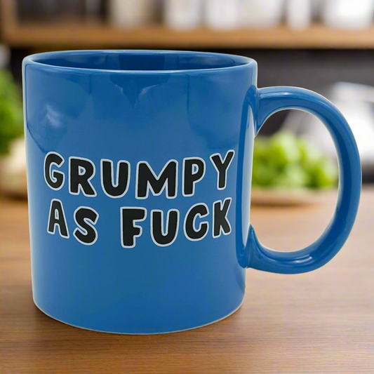 A blue ceramic mug with the text 'GRUMPY AS FUCK' written in black.