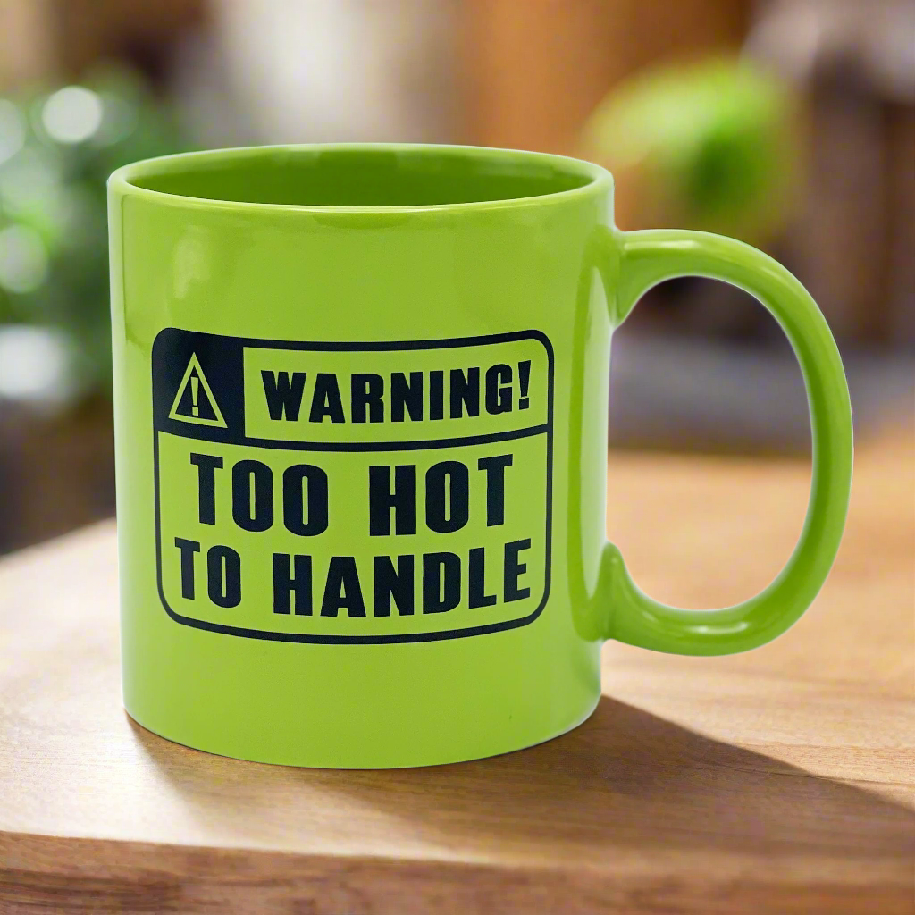 A green ceramic mug with a warning label text 'WARNING! TOO HOT TO HANDLE' printed on it.