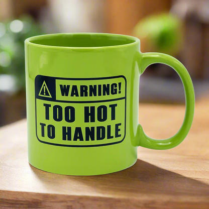A green ceramic mug with a warning label text 'WARNING! TOO HOT TO HANDLE' printed on it.