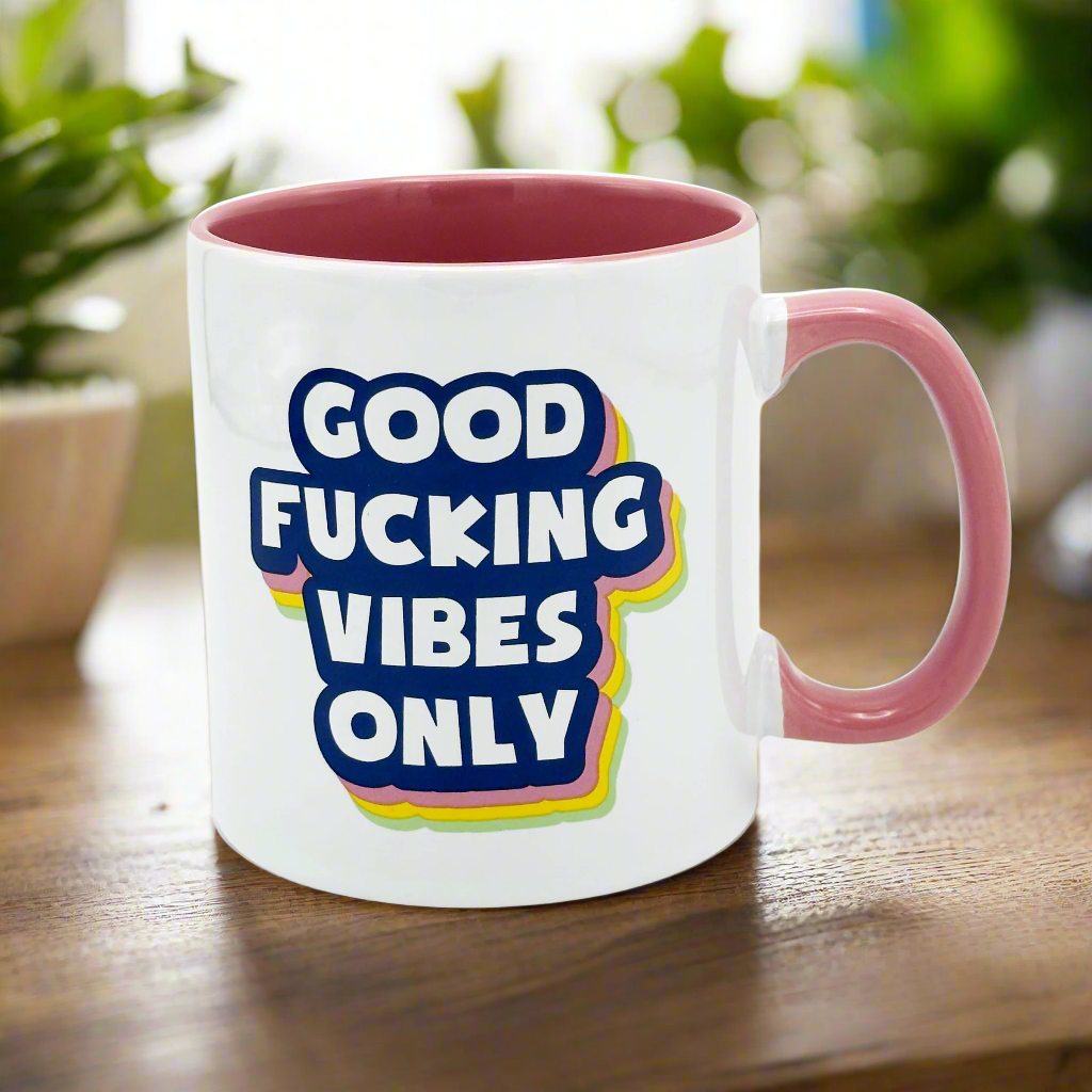 A large white mug with 'Good Fucking Vibes Only' printed in colorful letters on the front, with a pink handle.