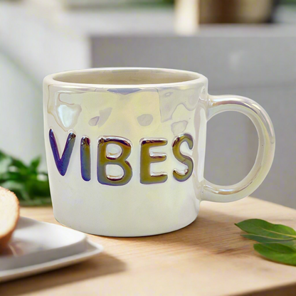 A white ceramic mug with the word 'VIBES' printed in gold letters on the side.